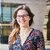 A portrait of image of Annina Kaltenbrunner. Annina wears a floral dress, a pair of black glasses.