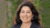 Smiling woman with long dark hair and blazer against blurred green foliage