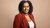 A portrait photo of Mikal Tseggai, where a red blazer and white top against a brown background