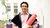 Dr Anderson Macedo de Jesus holds his PhD diploma in this portrait photo. He wears a coral shirt and is draped doctorate graduate regalia