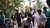 Group of people clapping and dancing outdoors by palm trees.