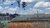 Sneakers dangling from a wire above corrugated metal roofs and a brick wall under a cloudy sky