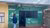 Black woman in blue jacket and jeans standing outside a green hut with Coalition of Grassroot Women Initiative written on the wall