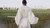 Man in white kimono-style robe standing in grass facing large white block letters