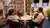 Three people seated around a round table with microphones, camera operator in studio