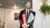 Young man in suit smiling while holding a red diploma tube indoors