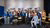Group of twenty conference attendees posing in a classroom with posters on the wall.