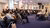 Business audience seated in a conference room listening to a speaker at lectern.