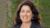 Smiling woman with long dark hair and blazer against blurred green foliage