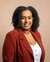 A portrait photo of Mikal Tseggai, where a red blazer and white top against a brown background