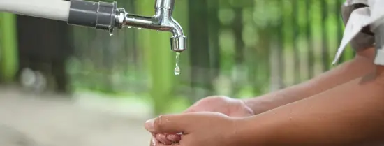 Child reaching hands forward to drink water from faucet