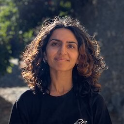 A women with dark brown hair and a long sleeve black shirt standing in nature