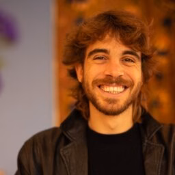 Man in a black tea and brown overcoat smiling