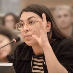 Woman raising her hand while seated at a conference table microphone