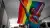 Person walking in front of a large group holding rainbow Pride flag above their head